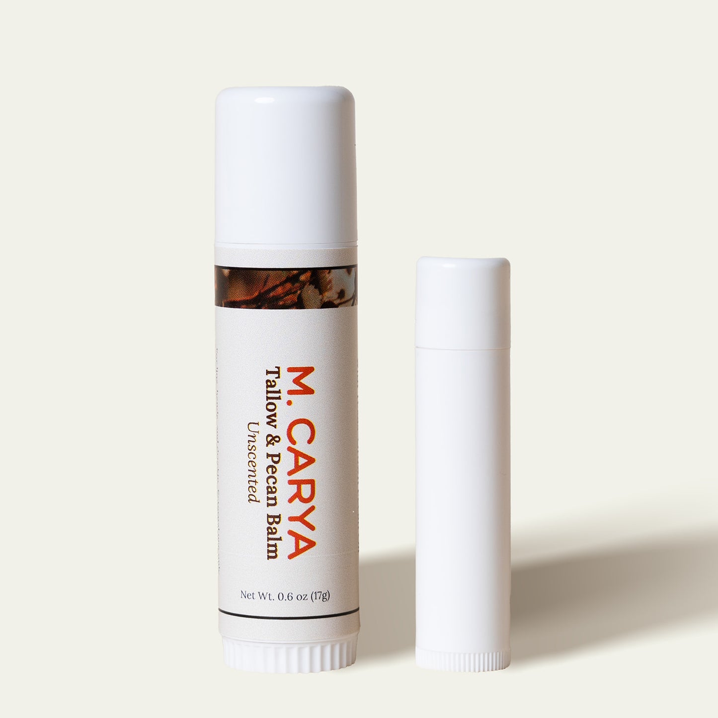 One M. Carya tube comparing its size to the typical white .15 oz balm tube.